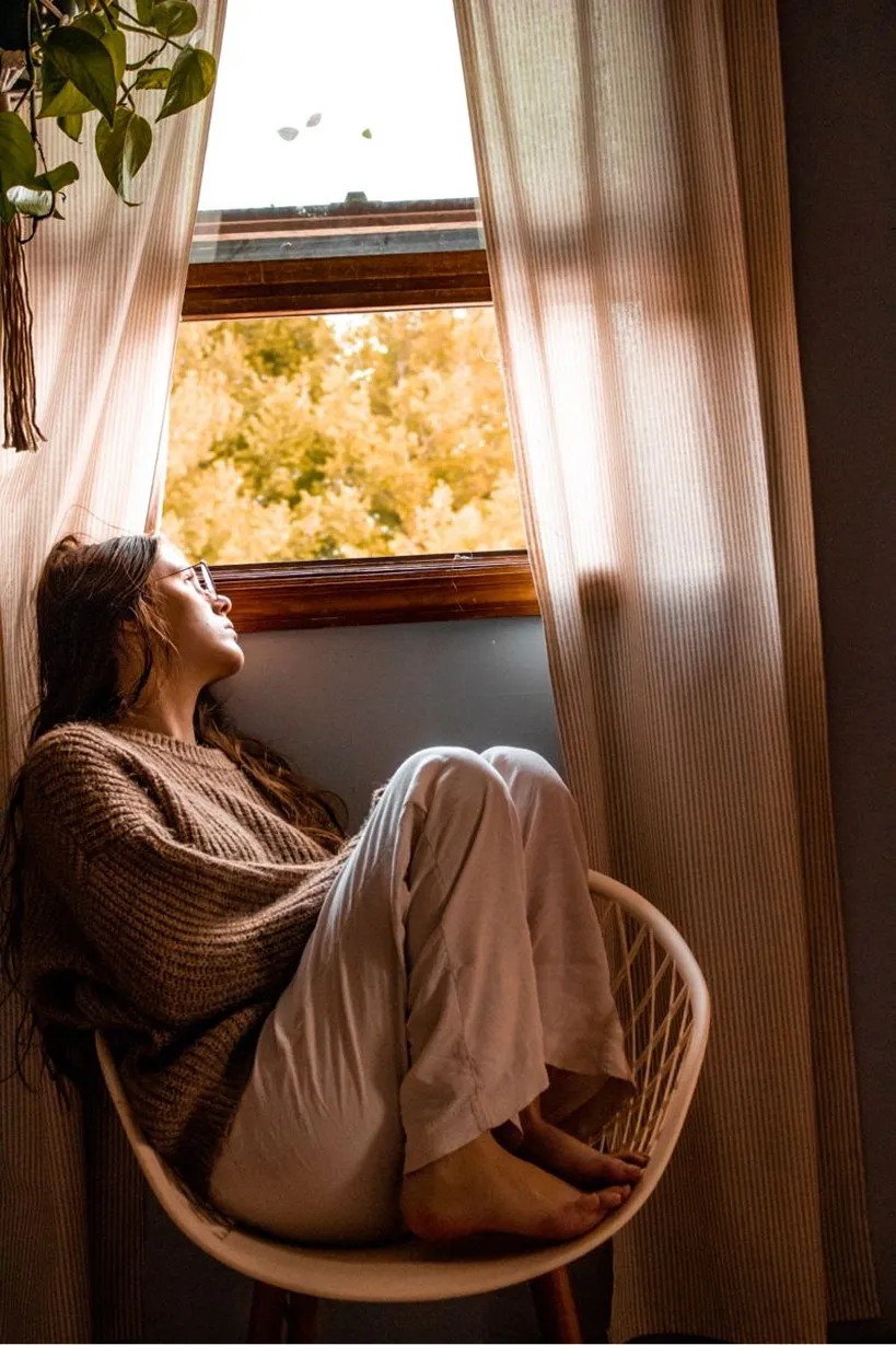 A woman sitting by a bright window, lost in thought