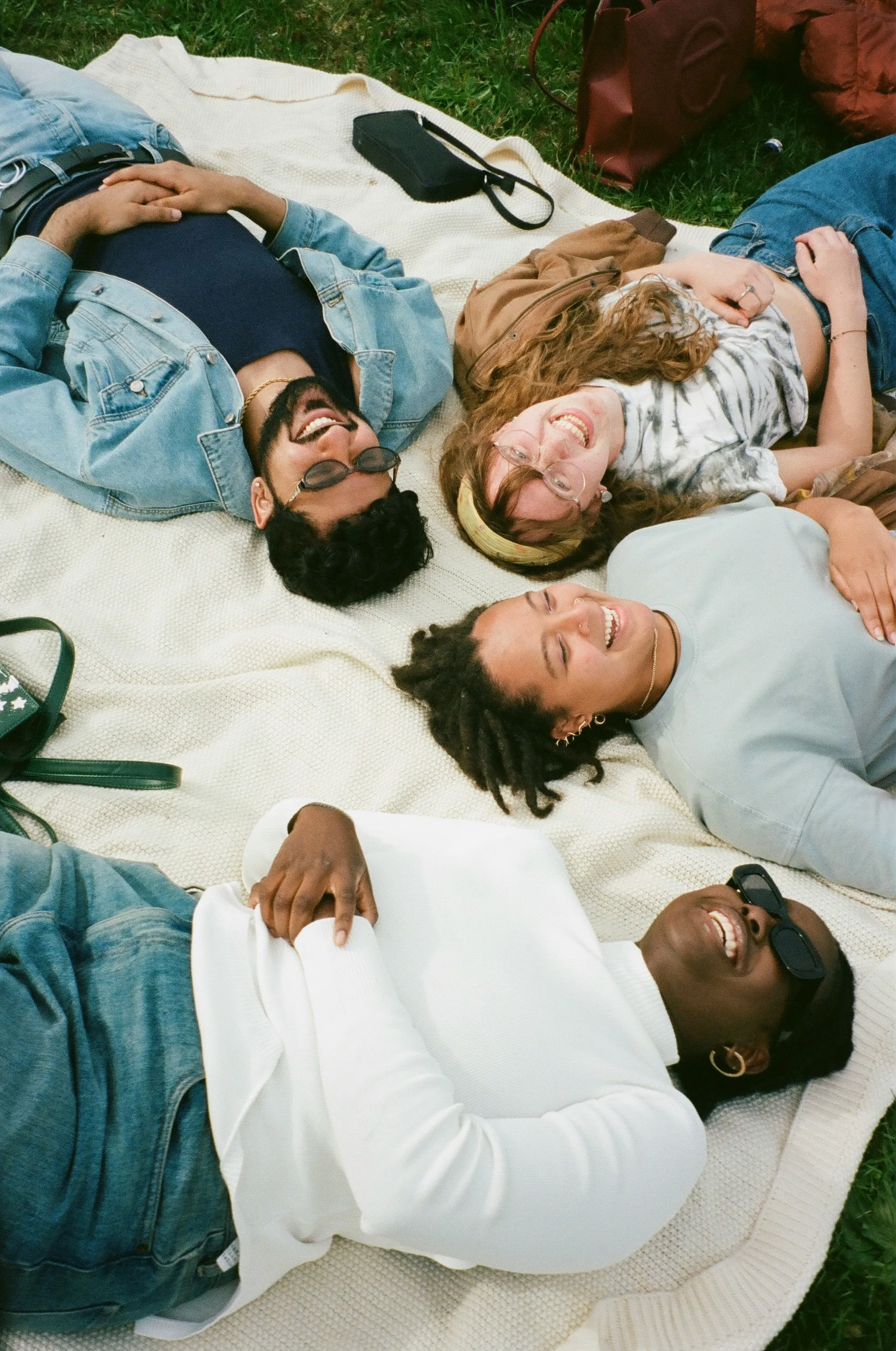 Four friends lying on a blanket in a park, laughing together