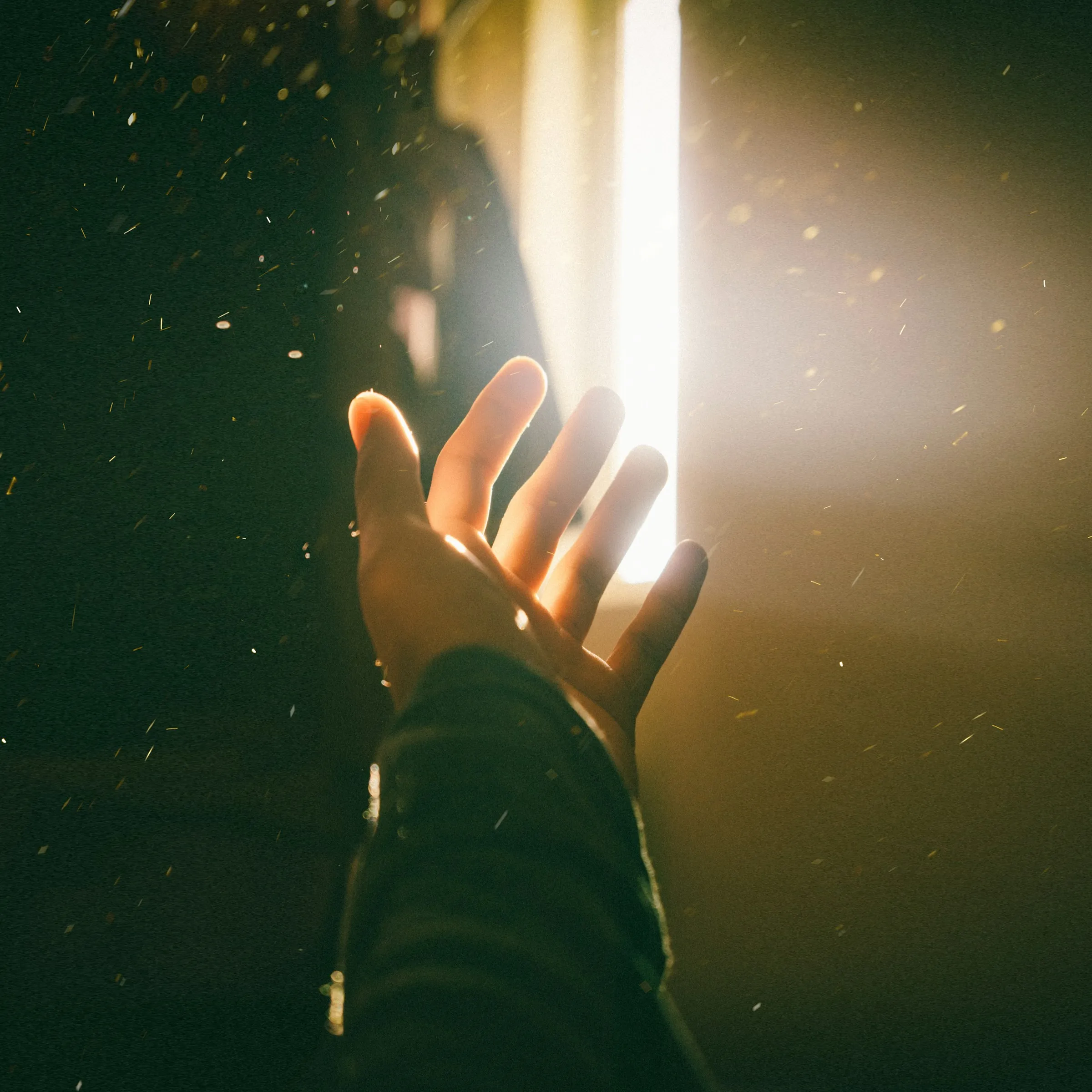 A hand reaching toward warm light through a window